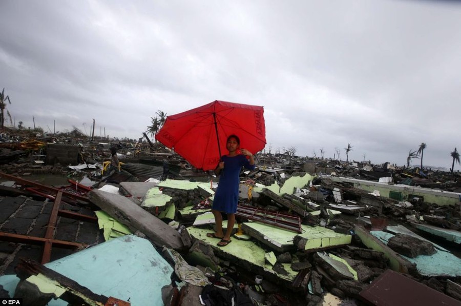 A woman holds her umbrella stands on debris of houses in Tacloban