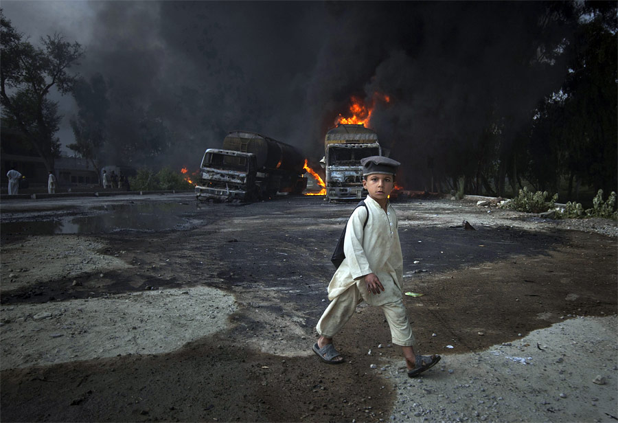 Пакистанский школьник идет мимо взорванных автоцистерн НАТО в Новшере. © Adrees Latif/Reuters