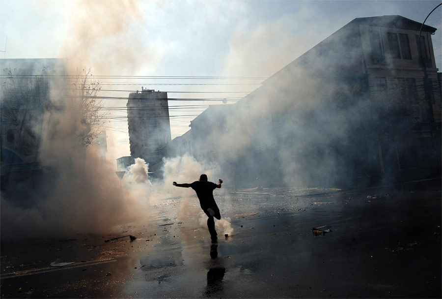 Демонстрант пинает газовую гранату во время антиправительственных выступлений в Вальпараисо, Чили. © Nano Rodriguez/Reuters