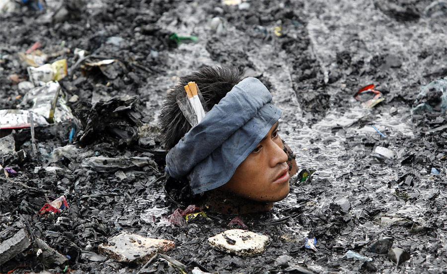 Филиппинец ищет ценные вещи в воде, заполненной мусором после крупного пожара в Маниле. © Erik de Castro/Reuters