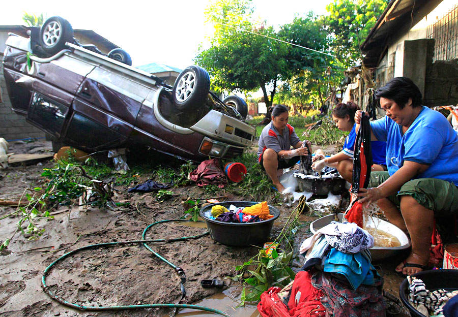 Пострадавшие от тропического шторма «Ваши» на юге Филиппин стирают одежду рядом с перевернутым автомобилем. © Erik De Castro/Reuters