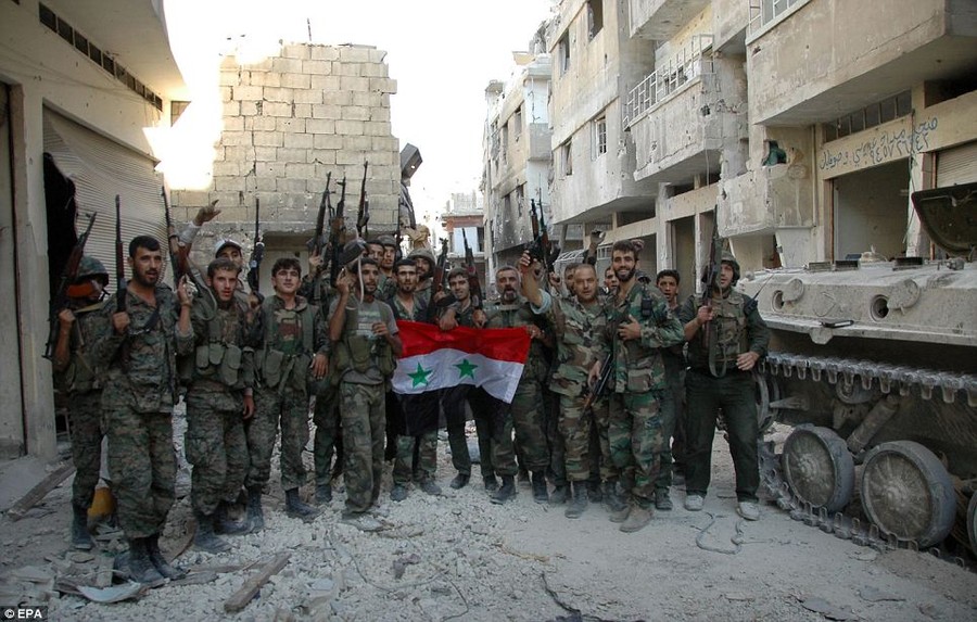 Victory? Syrian soldiers pose for a photo while holding the Syrian flag in al-Khalidyya neighborhood which they claim to have secured