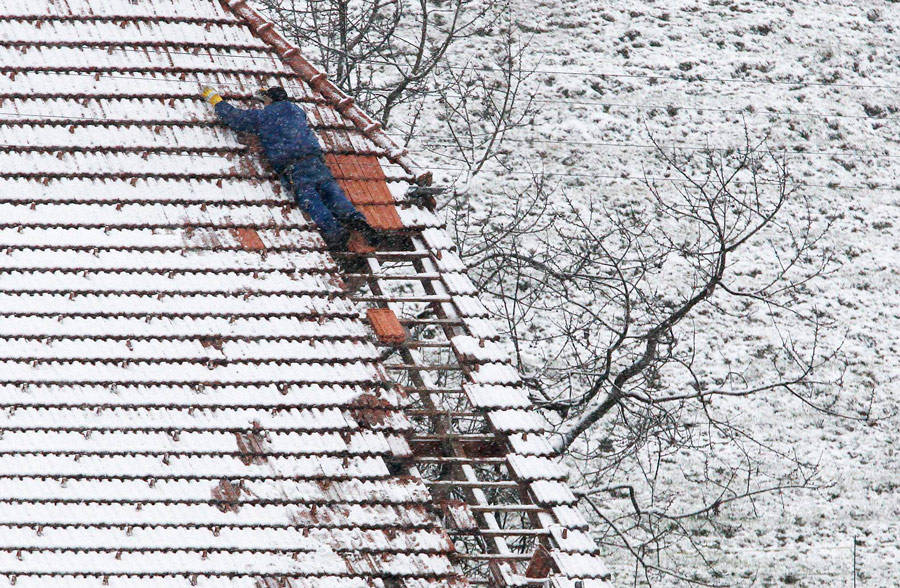 Кровельщик ремонтирует поврежденную крышу дома после шторма в пригороде Берна в Швейцарии. © Pascal Lauener/Reuters