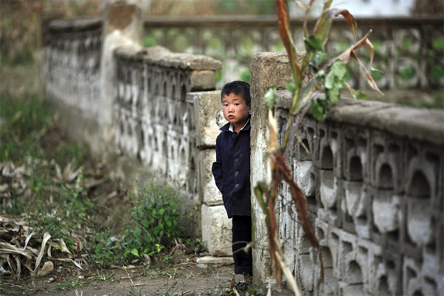 Мальчик выглядывает из-за ограды в колхозе Сокса-Ри, пострадавшему от недавних наводнений. © Damir Sagolj/Reuters