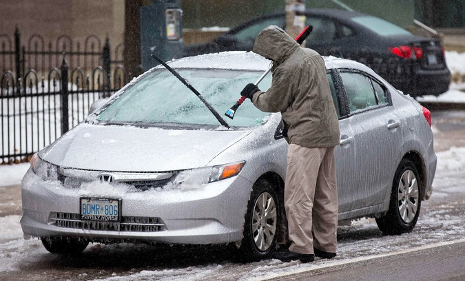 Мужчина счищает лед со своей машины.