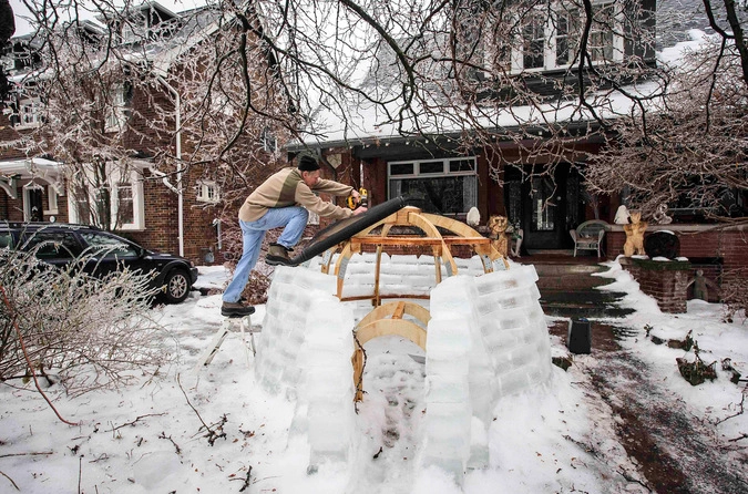 Мужчина строит иглу на лужайке перед своим домом.