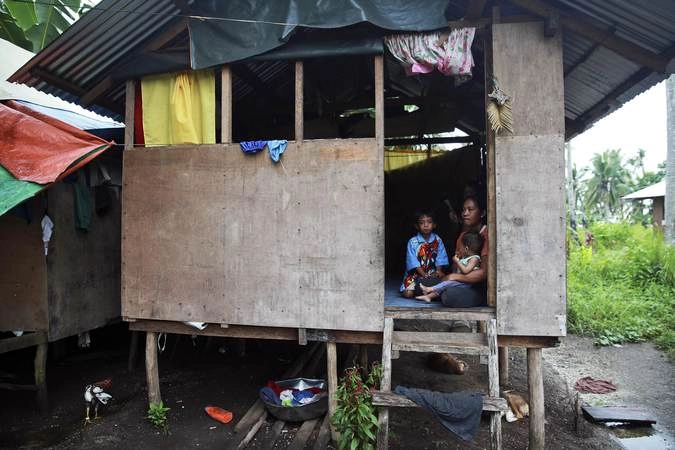Элизабет Карамол со старшим сыном и её годовалым ребёнком на пороге перестроенного после тайфуна дома в Марабуте.