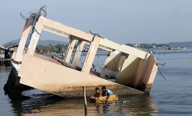 Мальчики на самодельной лодке возле каркаса дома, разрушенного во время тайфуна год назад.