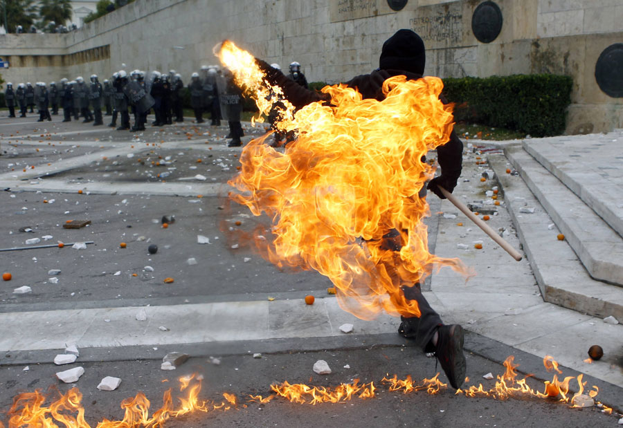 Участник акции протеста в Афинах кидает зажигательную бомбу в полицейских. © YANNIS BEHRAKIS/Reuters