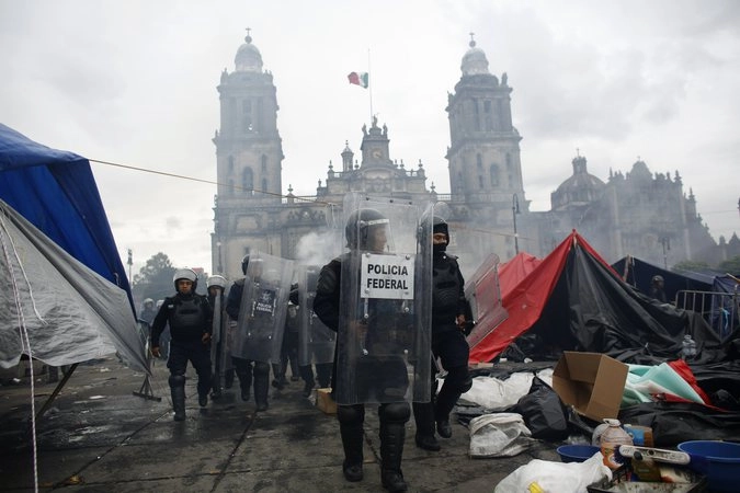 Полицейские идут перед собором в Мехико, разгоняя демонстрантов, выступающих  за радикального президента Энрике Пена Ньето.