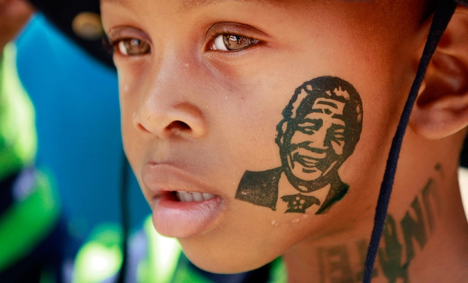  Мальчик с изображением Нельсона Манделы на лице стоит в очереди, чтобы проститься с бывшим президентом в городе Претория.