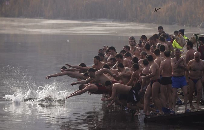 Мужчины прыгают в озеро в попытке схватить деревянный крест. 