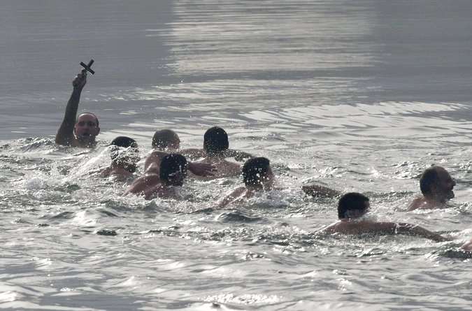 Болгарин Вячеслав Борисов держит деревянный крест. Он плавает в водах озера в день Богоявления в Софии.