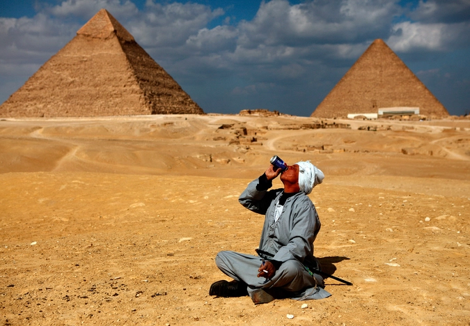 Мужчина пьет газированный напиток у пирамид в Гизе. 13.02.2011