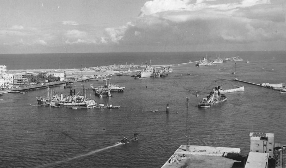 Вход в гавань Порт-Саида, начало ноября 1956 года. Вид на север со стороны Порт-Фуада, на заднем плане — Рыбная гавань и Западный мол. Хорошо видно, что из-за затопленных на фарватере судов крупные транспорты не могут войти в гавань и подойти к причалам. На переднем плане — британское спасательное судно «Си Сальватор» ведёт судоподъёмные работы, у входа в Рыбную гавань стоит британская база подлодок «Форт» в окружении малых кораблей, дальше у мола видны плавмастерская «Ранпура» и штабное судно «Тайн» 