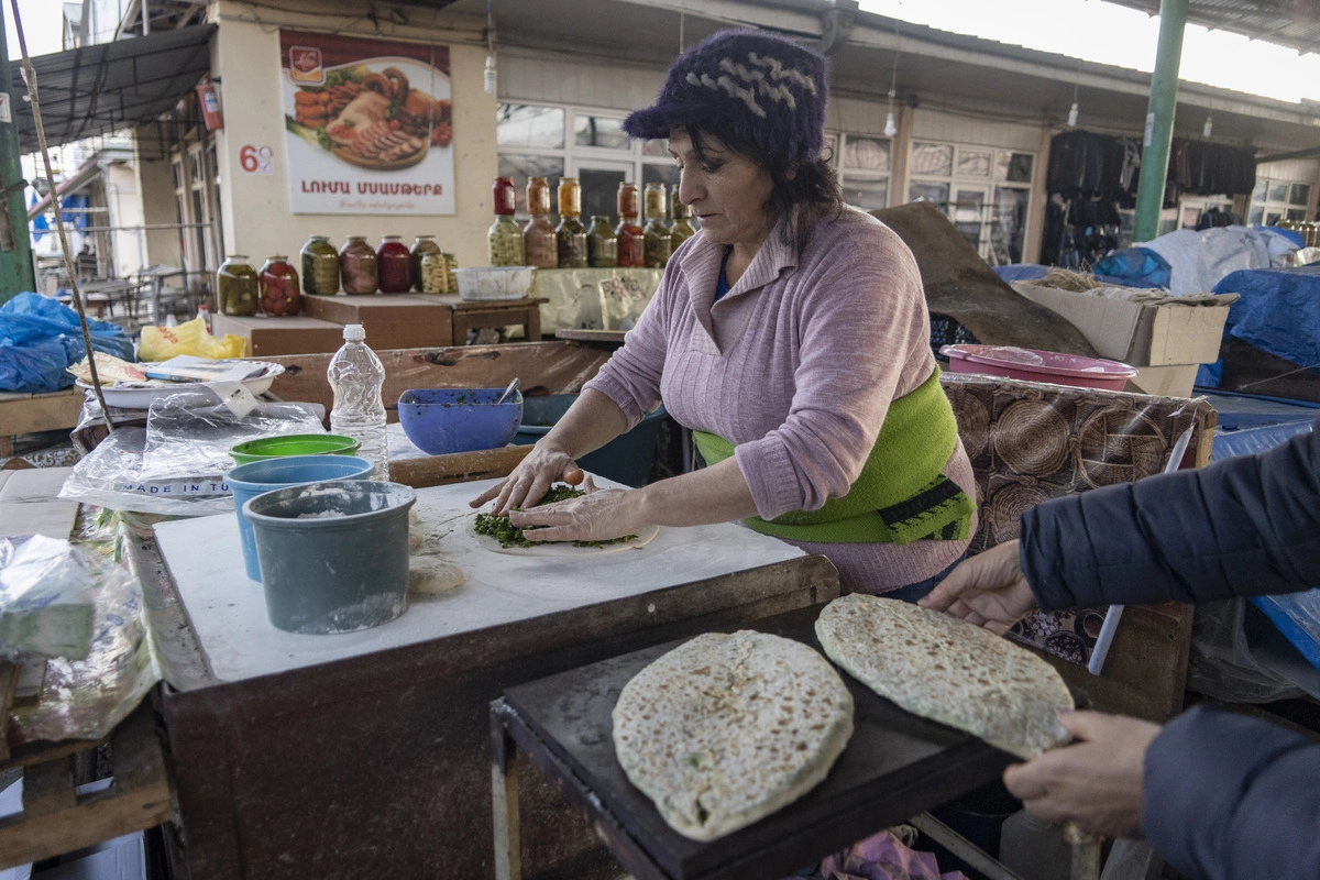 Женщина на рынке готовит традиционный пирог (лепёшка с зеленью 