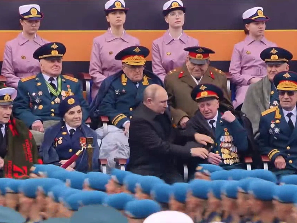 Владимир Путин помогает накинуть куртк ветерану Василию Пронину.