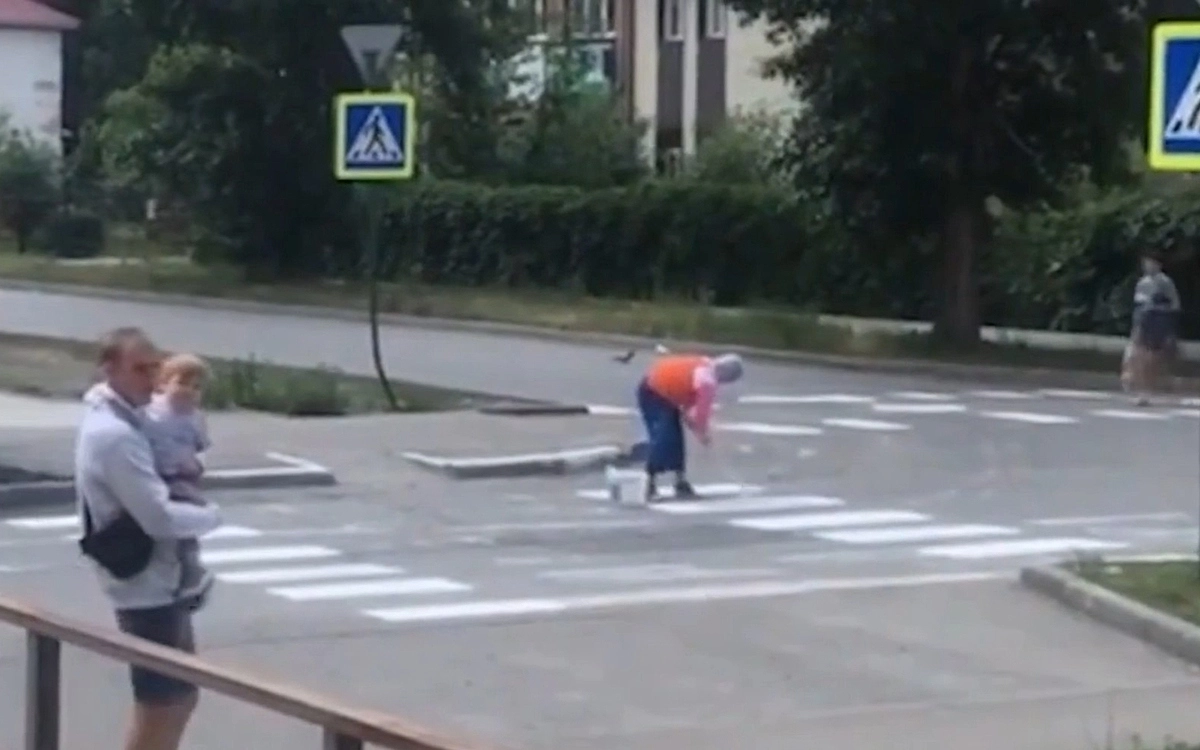Женщина взяла ведро белой краски, самодельную кисточку и перчатки, вышла на дорогу и принялась за работу